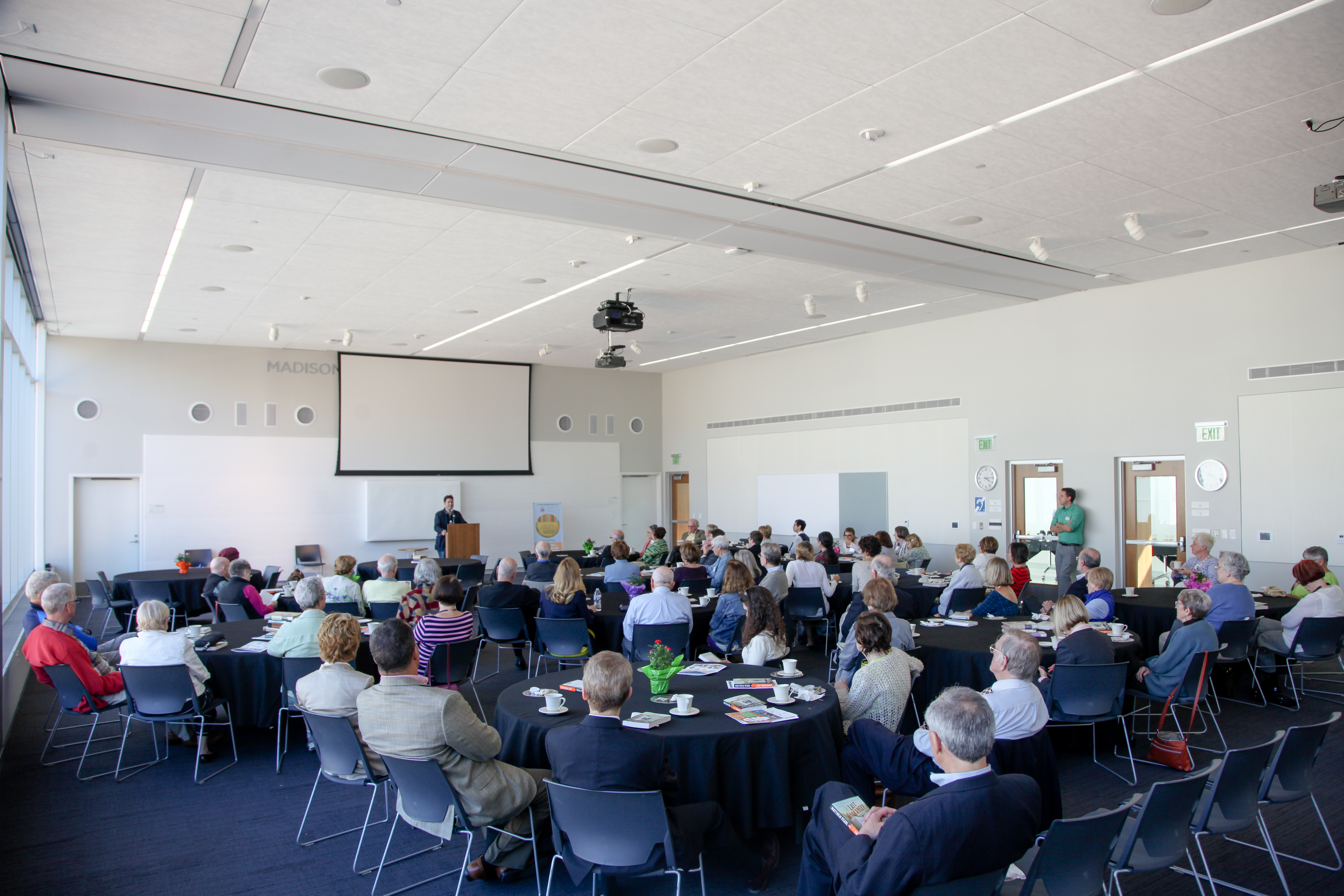 Groups of people sitting at round tables watching a speaker at a podium