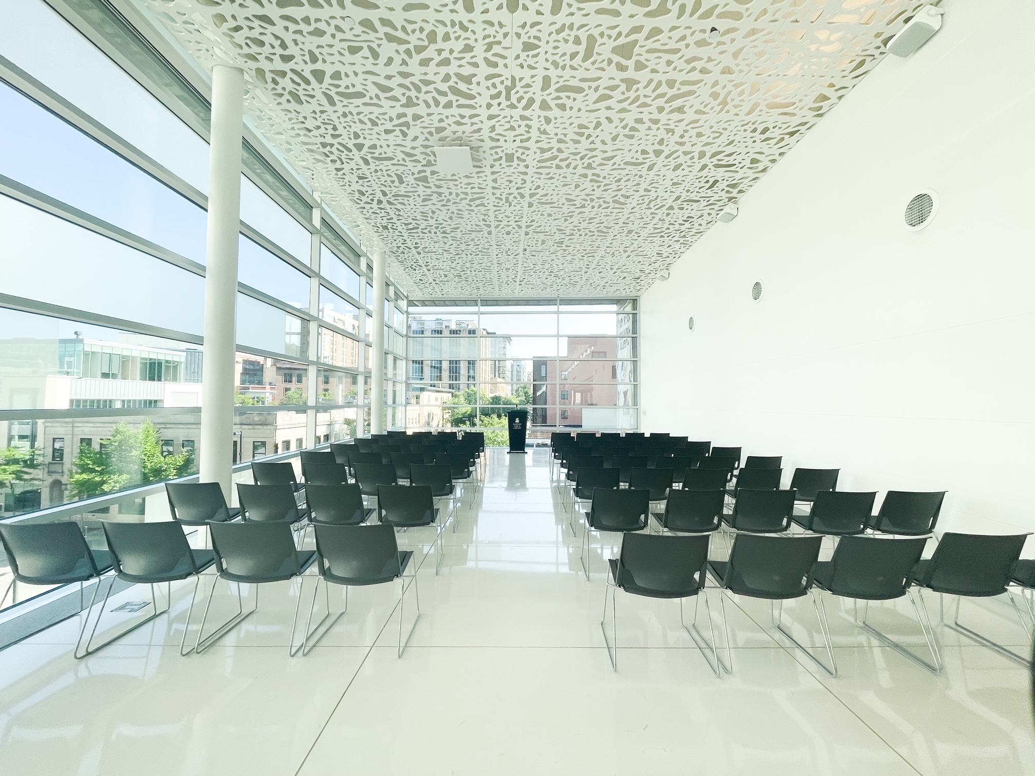 Chairs in rows on either side of center aisle facing a black podium in a room of windows