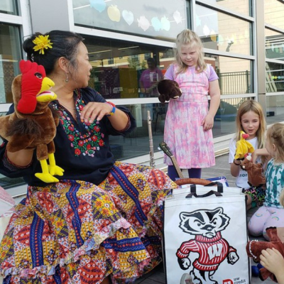 Children gathered around a woman, playing with puppets