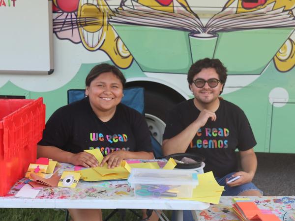 Two Dream Bus employees site behind a low table covered in art supplies in front of Madison Public Library's mobile library
