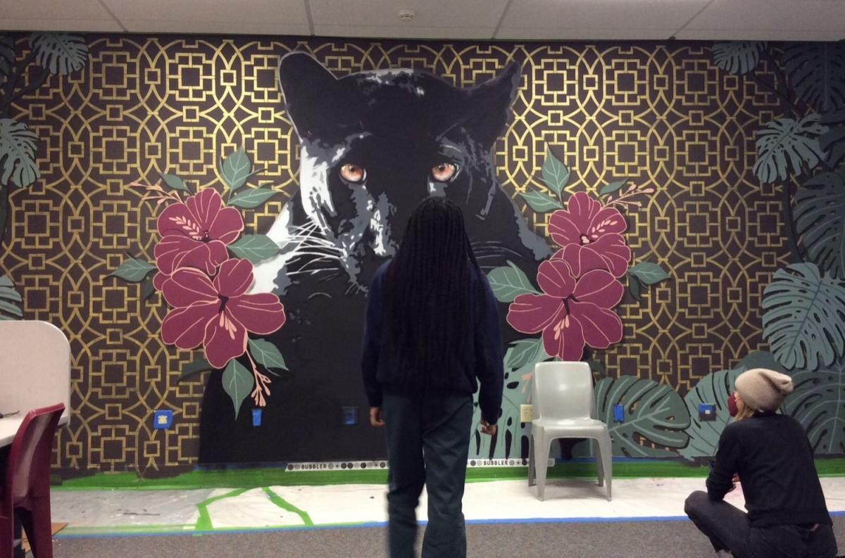Picture of Audifax sitting by a youth taking in the completed mascot mural in the Detention Center classroom.