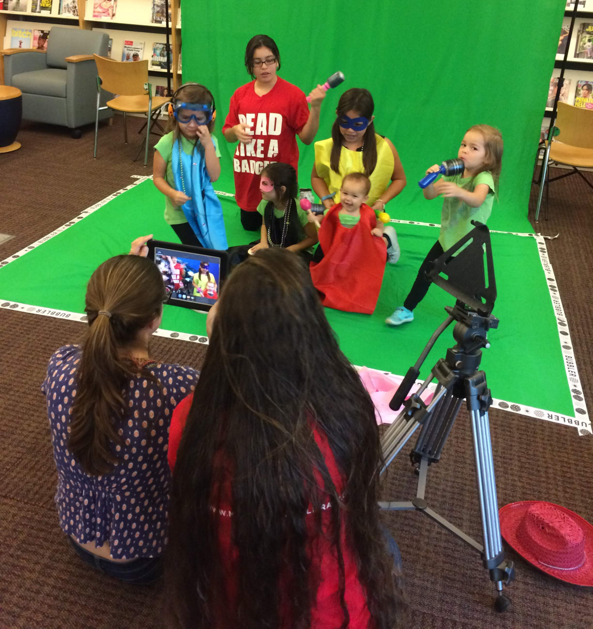 group of kids recording a music video at the library in front of a green screen