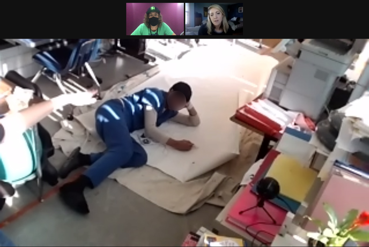 Picture of student working on mural canvas in jail classroom while connected to the artist on zoom.