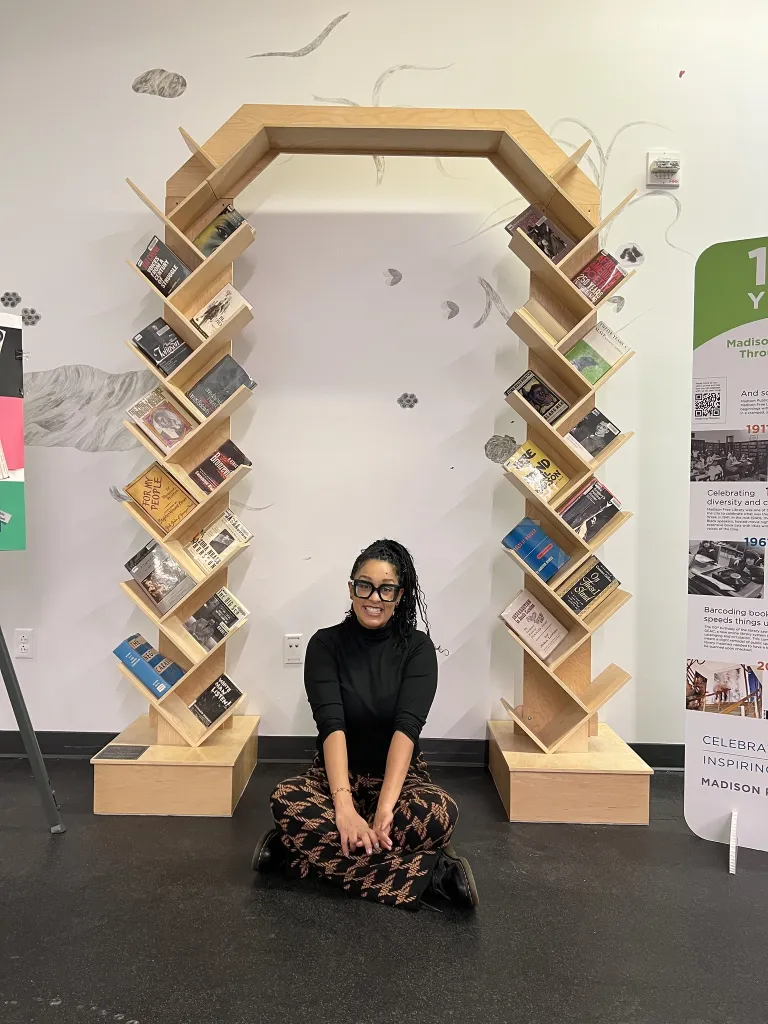 A woman sits in front of a wooden arched bookshelf with books on it