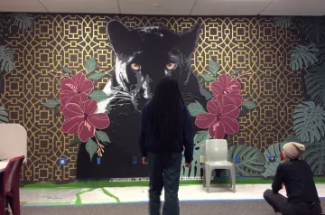 Audifax_Madison_Mural_Detention_Center.jpeg Picture of Audifax sitting by a youth taking in the completed mascot mural in the Detention Center classroom.