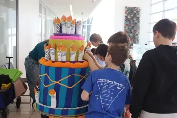 Kids gather around a non-edible cake to add paper candles with testimonials written on them for Madison Public Library's 150th Anniversary