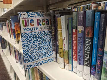 Copy of the WE READ Youth Voices Anthology pulled slightly off of a book shelf at the library