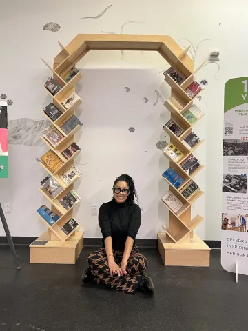 A woman sits in front of a wooden arched bookshelf with books on it