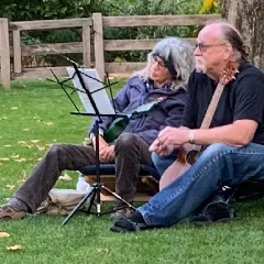 A photo of the two members of Tite2Nite, sitting outside on the grass with their instruments