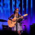 A photo of carisa playing acoustic guitar on a stage A photo of carisa playing acoustic guitar on a stage