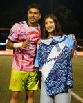 Soccer player and young girl stand side-by-side on a field. The girl is holding up a jersey in front of her
